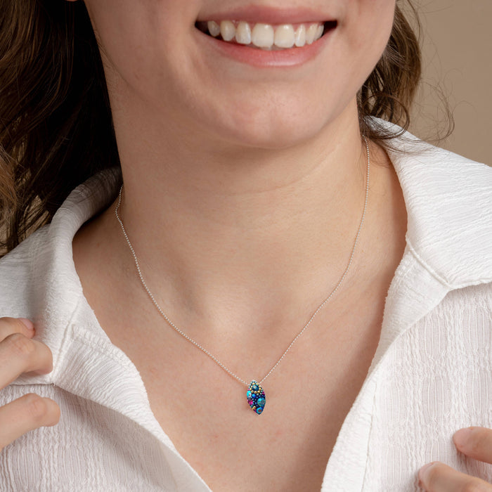 A model wearing the Bijou Seed Necklace by Mosaico Jewels, highlighting the colorful seed pendant against a white shirt, emphasizing elegance and style.