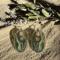 Camellias Stained Glass Resin Earrings by Wild Lupine Folkcraft, showcasing a stainless steel botanical design infused with soft-colored resin, beautifully catching the light against a natural background.