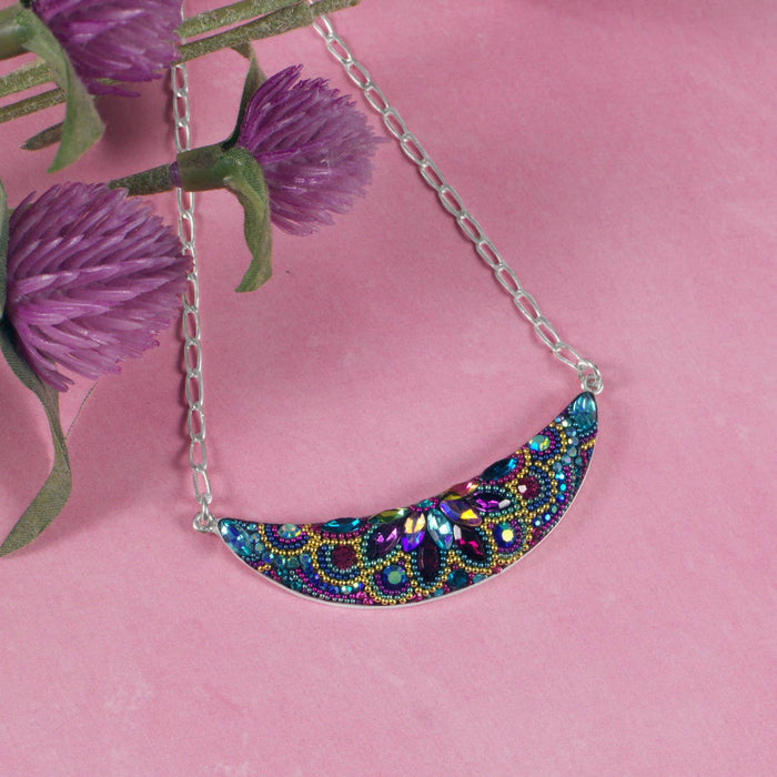 Vibrant Luna Crystal Necklace by Mosaico Jewels showcasing intricate beadwork in a crescent moon design against a pink background.
