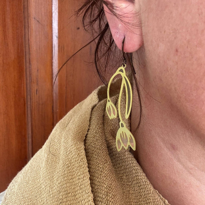 Close-up of a person wearing Snowdrop Stained Glass Resin Earrings from Wild Lupine Folkcraft. The earrings feature a unique design resembling snowdrop flowers, highlighting their lightweight and vibrant appearance.