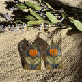 Tracery Stained Glass Resin Earrings by Wild Lupine Folkcraft showcased against a textured background, highlighting the brass geometric botanical design and soft-colored resin stained glass.